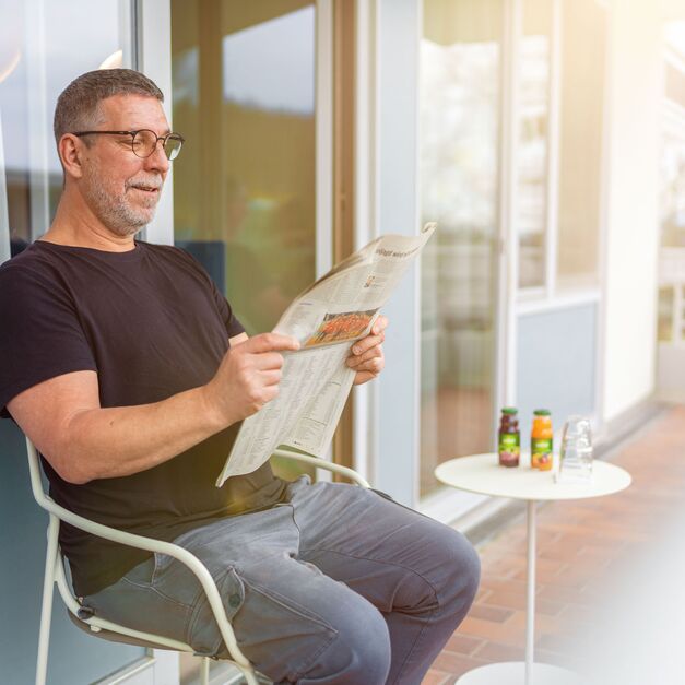 Patient sitzt auf dem Balkon und liest Zeitung