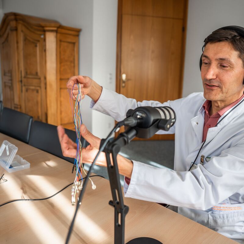 Arzt im Podcaststudio, er zeigt Goldnapf-Elektroden.