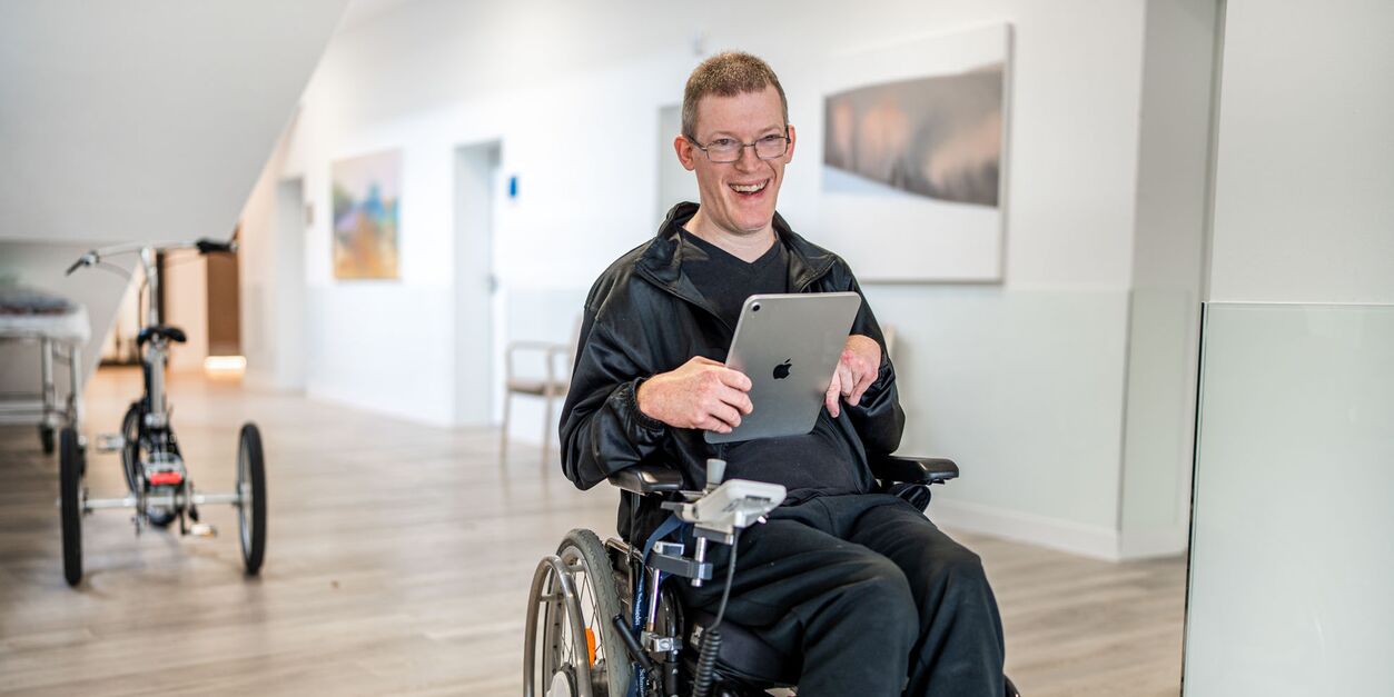 Patient im Rollstuhl, der ein Tablet hält, in einem Klinikflur