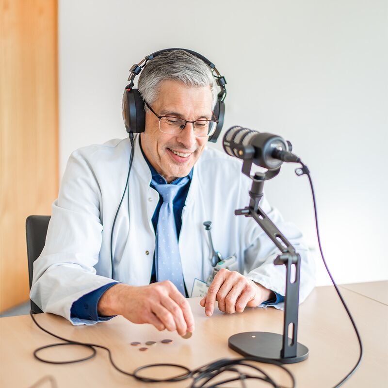 Arzt im Podcaststudio, er hält Münzen in der Hand.